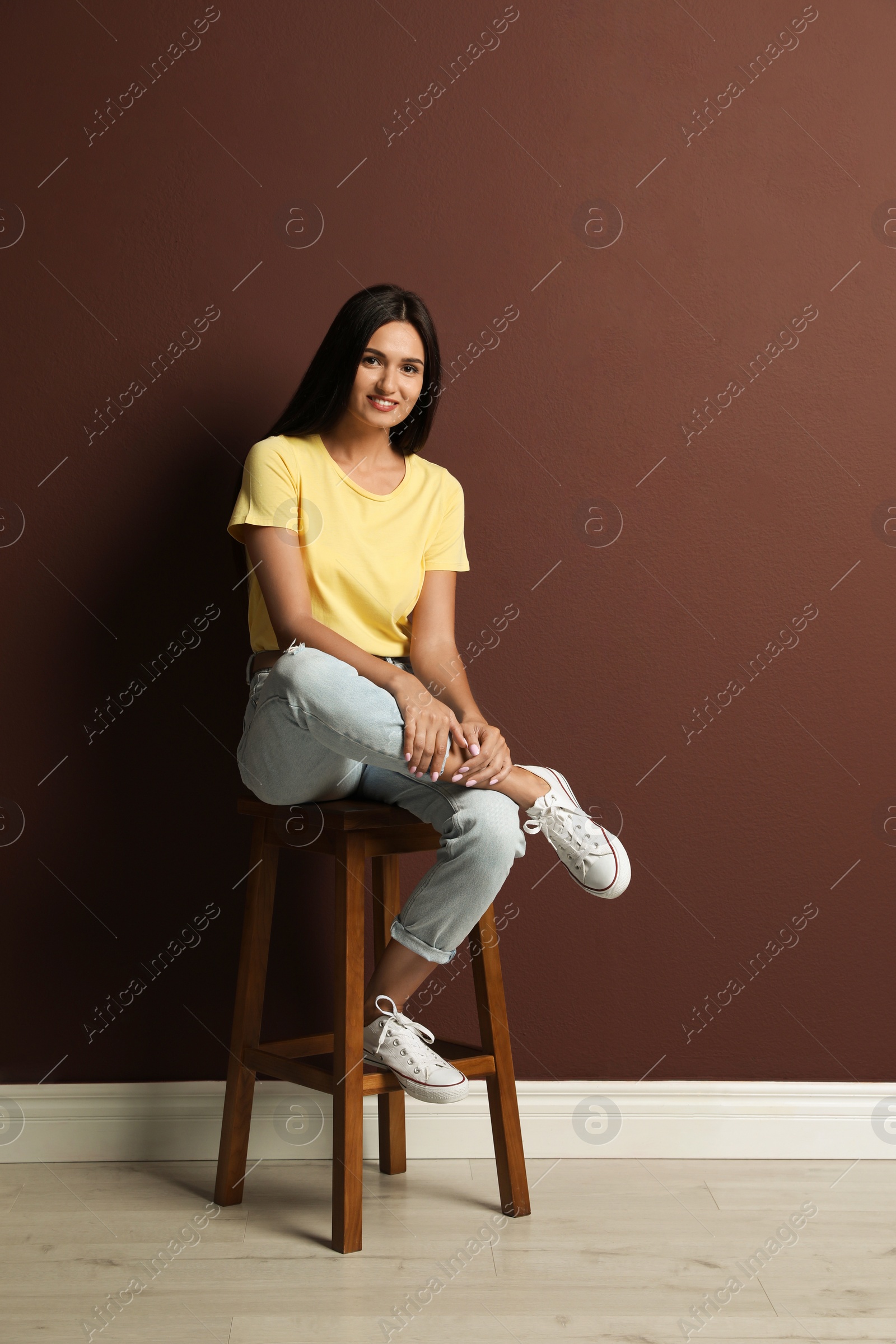Photo of Beautiful young woman sitting on stool near brown wall