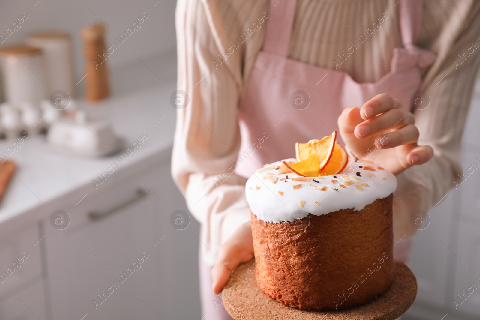 Photo of Young woman with traditional decorated Easter cake in kitchen, closeup. Space for text