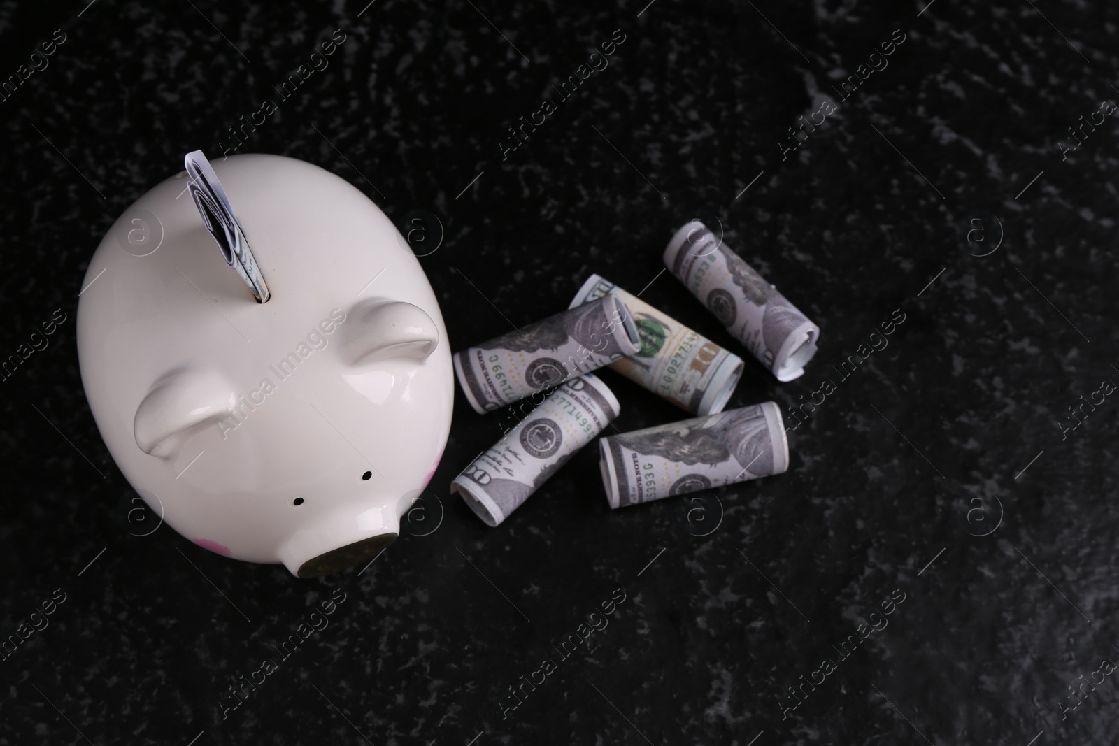 Photo of Financial savings. Piggy bank and dollar banknotes on black textured table, flat lay