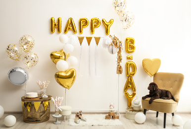 Photo of Chocolate Labrador Retriever and phrase HAPPY BIRTHDAY made of golden balloon letters in decorated room