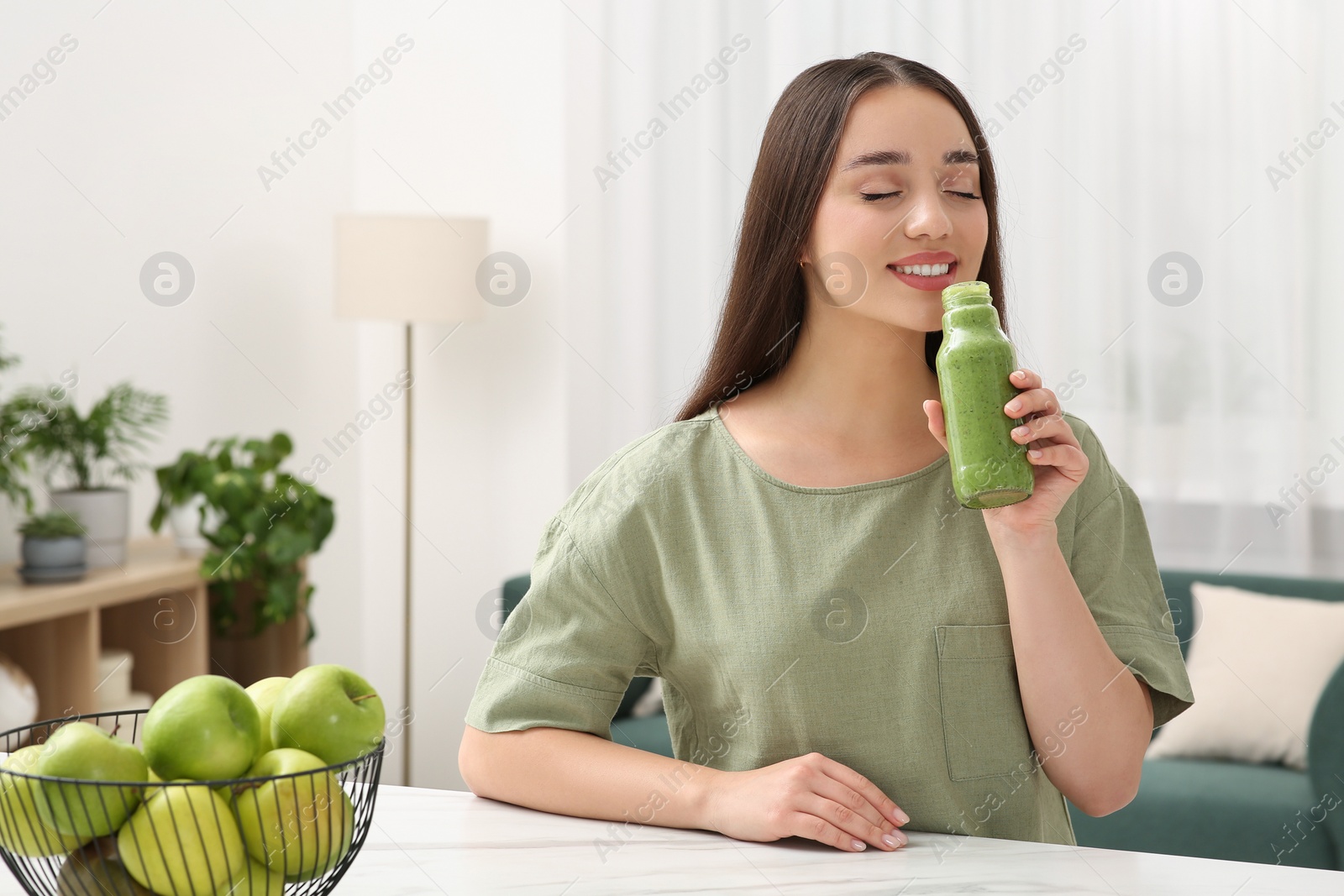 Photo of Beautiful young woman drinking delicious smoothie at home