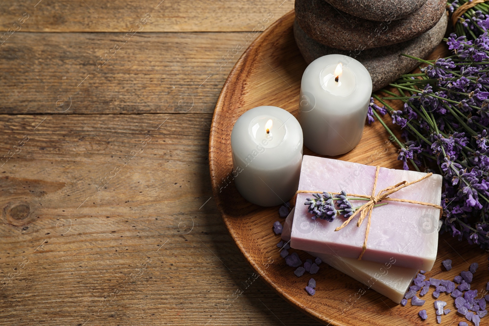 Photo of Burning candles, stones, soap bars and lavender flowers on wooden table. Space for text