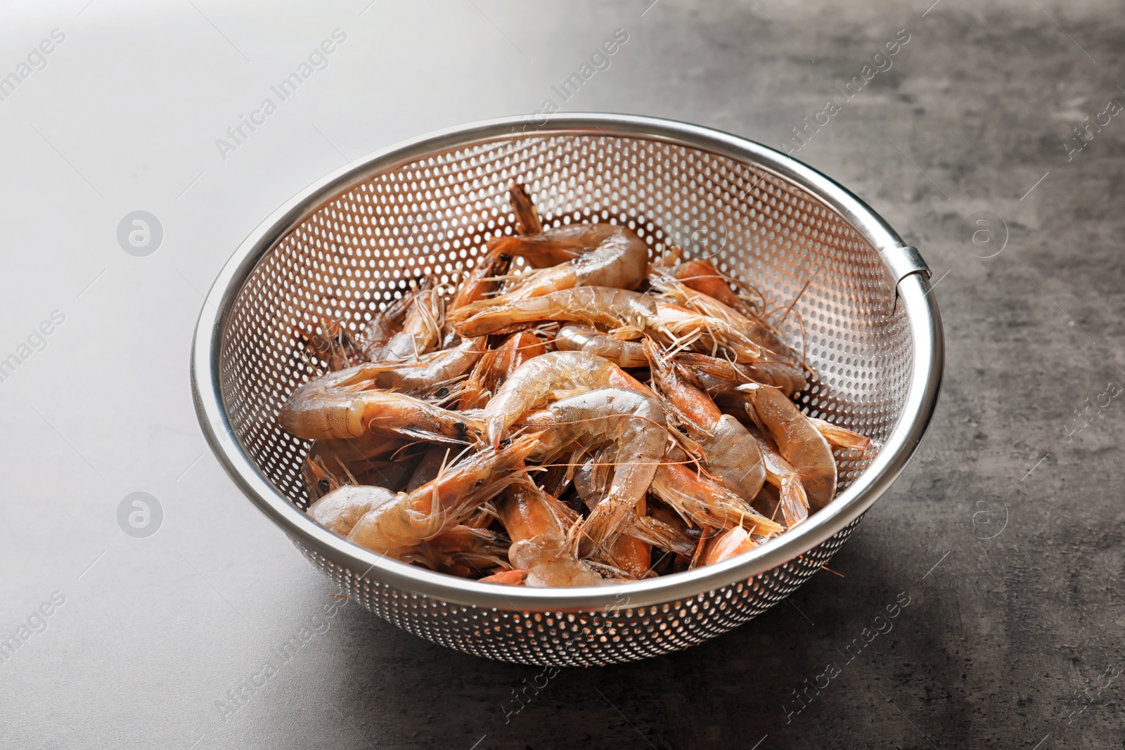 Photo of Colander with fresh shrimps on gray background