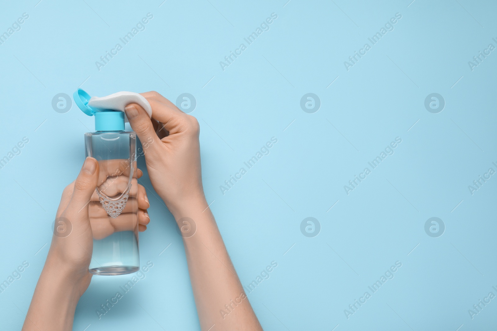 Photo of Woman pouring makeup remover onto cotton pad on light blue background, top view. Space for text