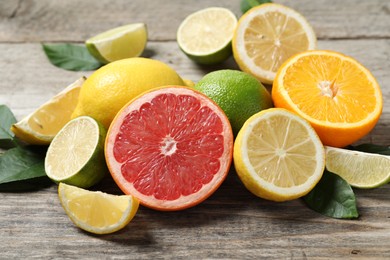 Photo of Different fresh citrus fruits and leaves on wooden table, closeup