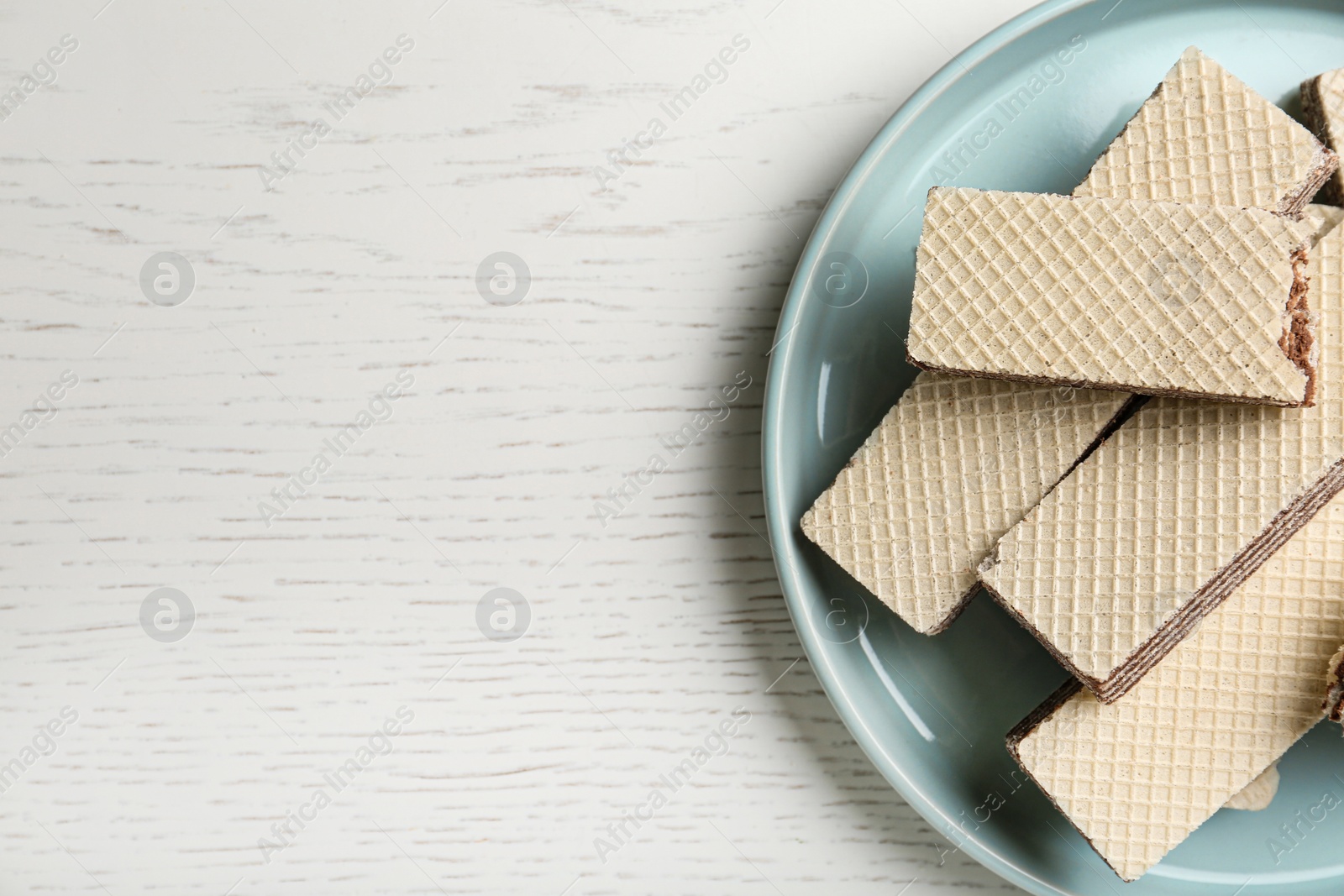 Photo of Plate of delicious crispy wafers with chocolate filling on white wooden table, top view. Space for text