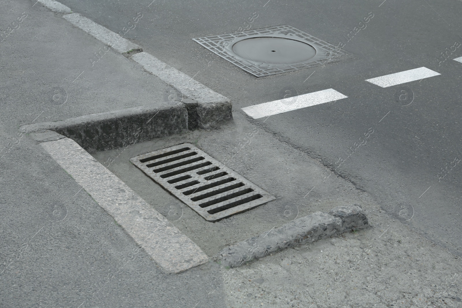 Photo of Metal drain grate and sewer hatch on asphalt outdoors