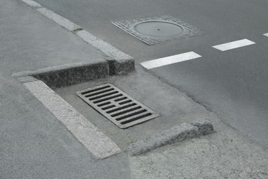 Photo of Metal drain grate and sewer hatch on asphalt outdoors