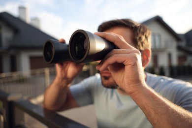 Concept of private life. Curious man with binoculars spying on neighbours over fence outdoors, selective focus