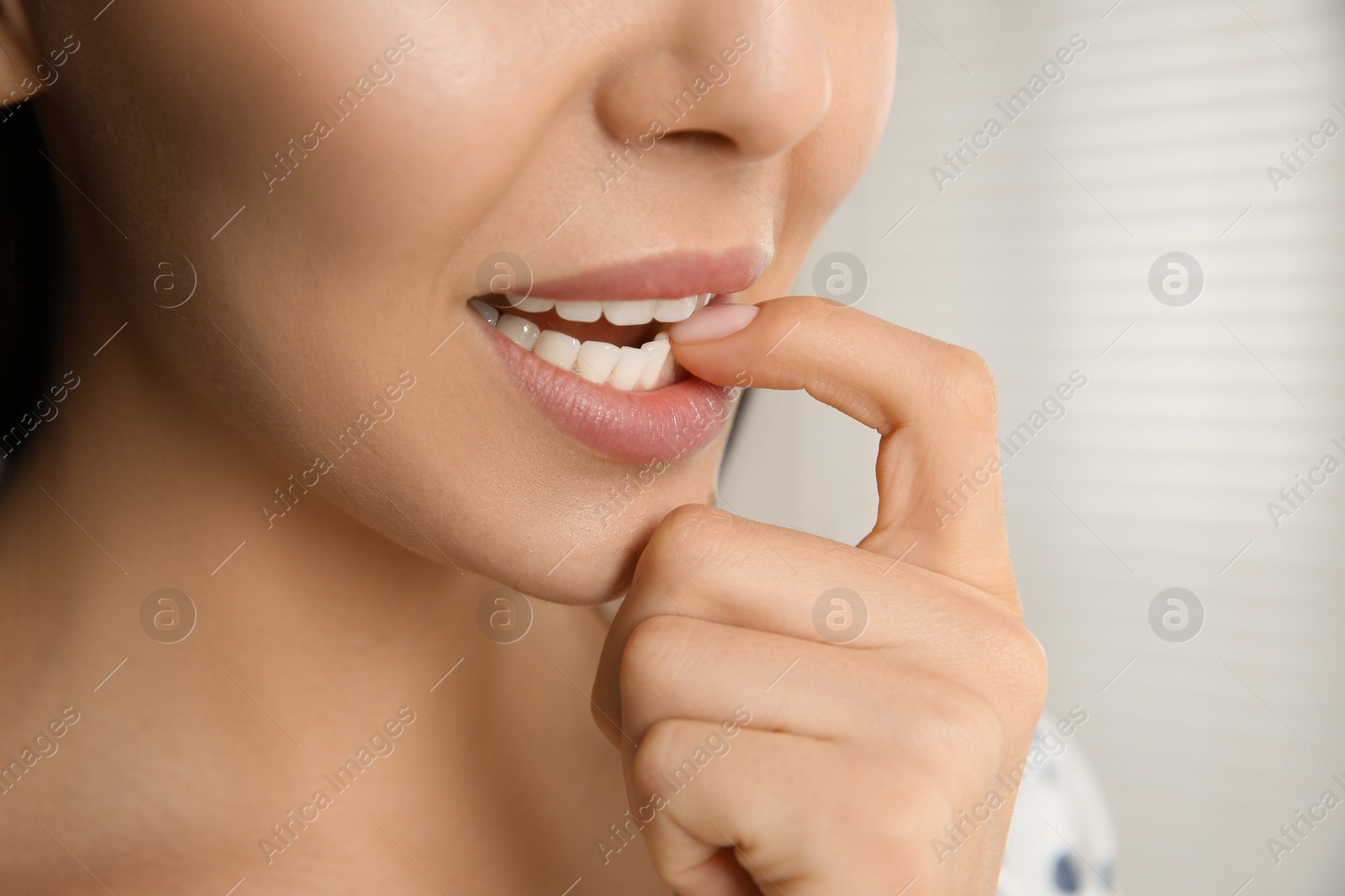 Photo of Young woman biting her nails on blurred background, closeup