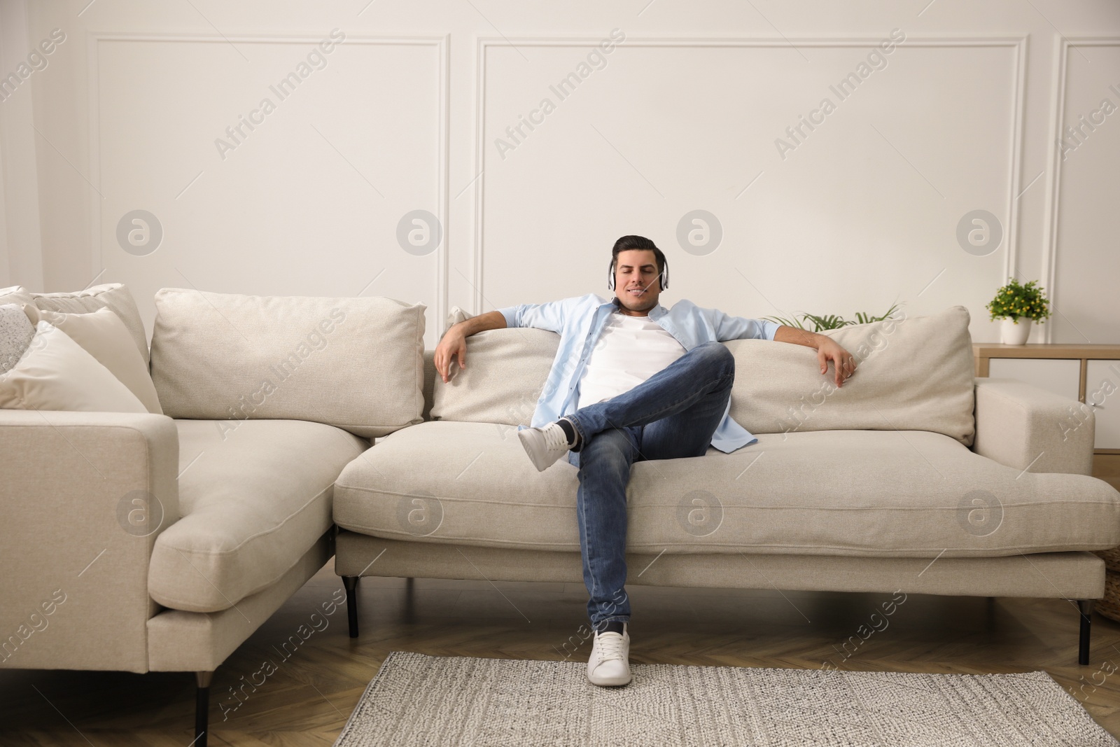 Photo of Man with headphones sitting on comfortable sofa in living room