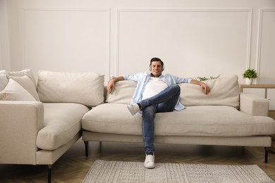 Photo of Man with headphones sitting on comfortable sofa in living room