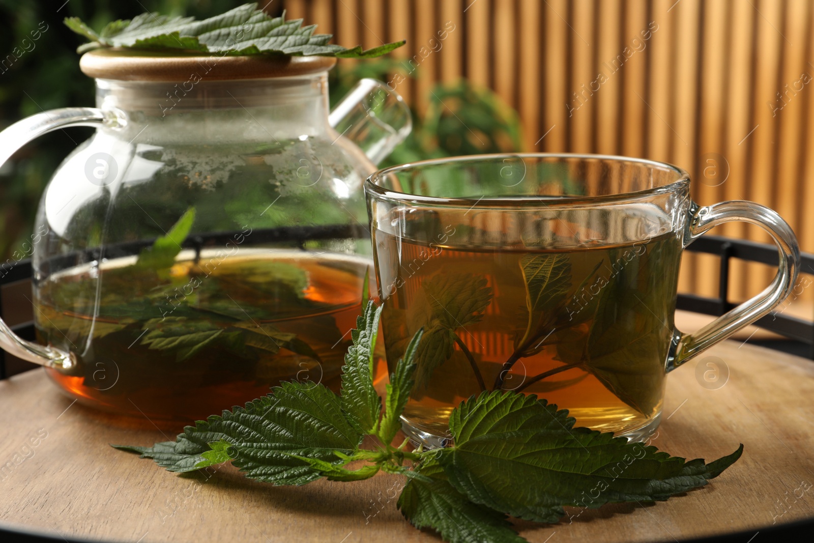 Photo of Aromatic nettle tea and green leaves on wooden tray, closeup