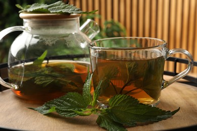 Aromatic nettle tea and green leaves on wooden tray, closeup