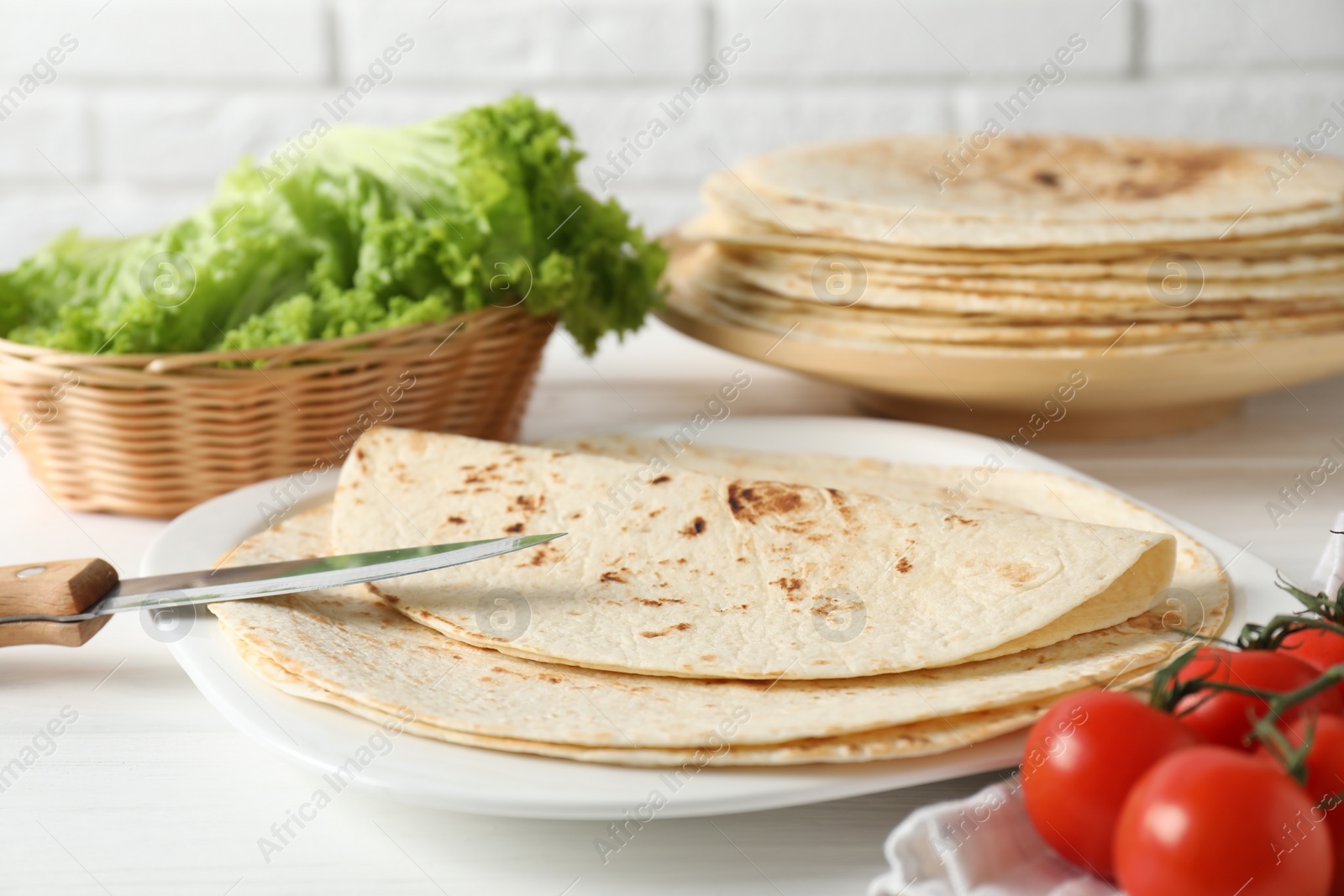 Photo of Tasty homemade tortillas, tomatoes, lettuce and knife on white wooden table