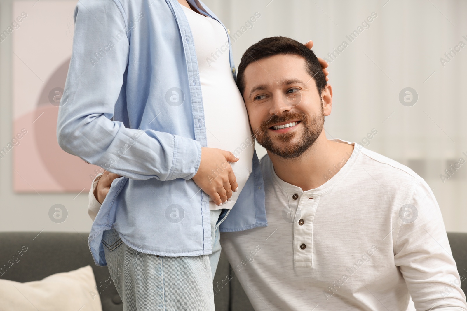 Photo of Happy husband listening pregnant wife's belly at home