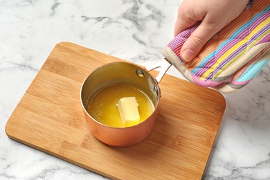 Woman holding saucepan with melting butter on marble background, closeup