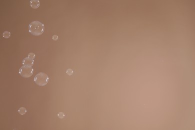 Photo of Many beautiful soap bubbles on light brown background. Space for text