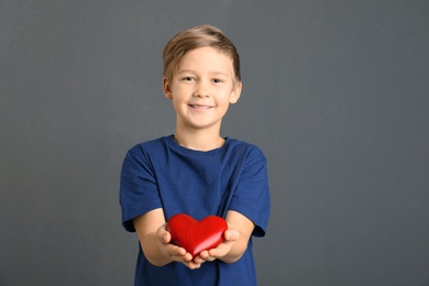 Cute boy holding wooden heart on grey background