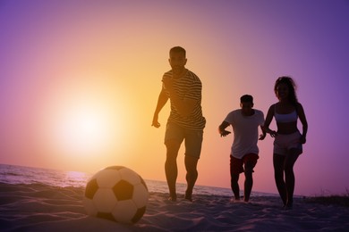 Friends playing football on beach at sunset