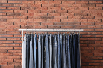 Rack with stylish jeans near brick wall