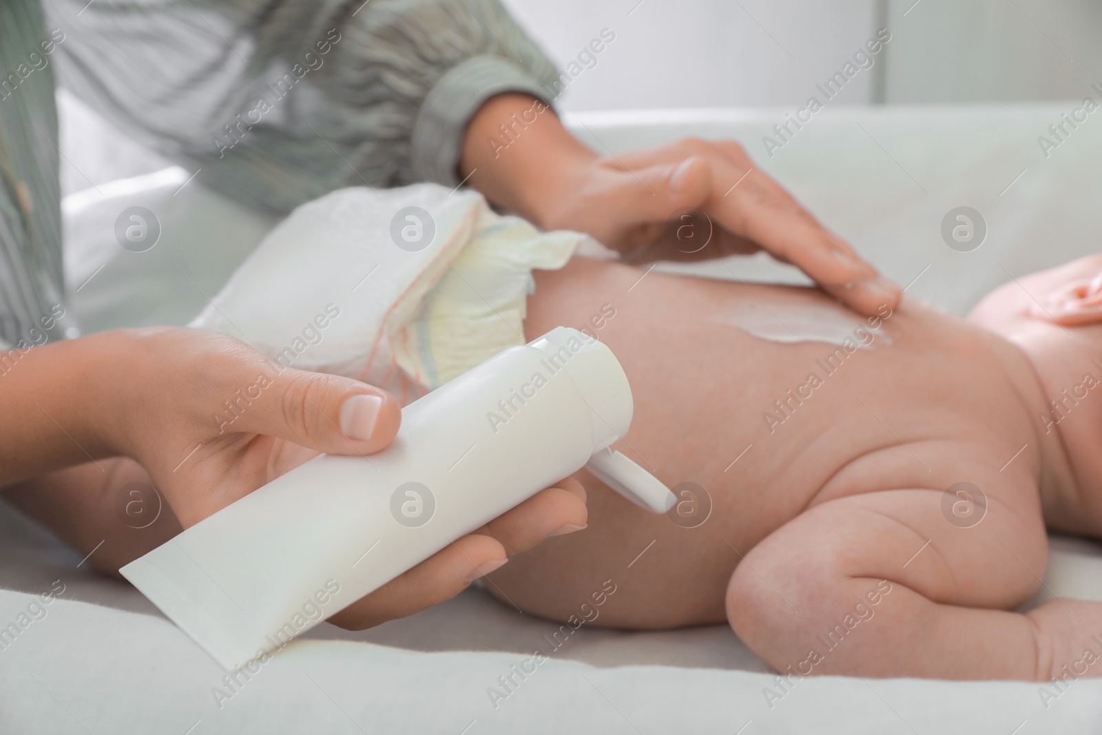 Photo of Mother applying moisturizing cream onto baby`s back on changing table, closeup