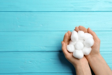 Woman holding cotton balls on color wooden background, top view. Space for text