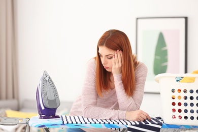 Tired housewife with clothes prepared for ironing at home