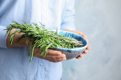 Photo of Young woman holding bowl of fresh rosemary, closeup