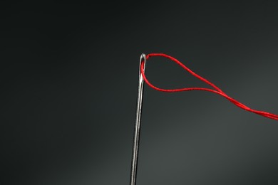 Photo of Sewing needle with red thread on dark background, closeup