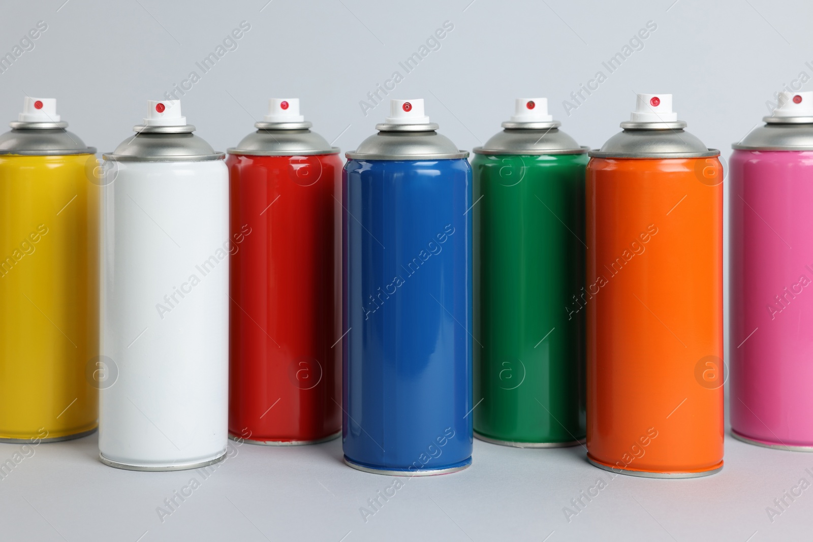 Photo of Colorful cans of spray paints on light grey background