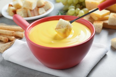 Dipping piece of bread into tasty cheese fondue at grey table