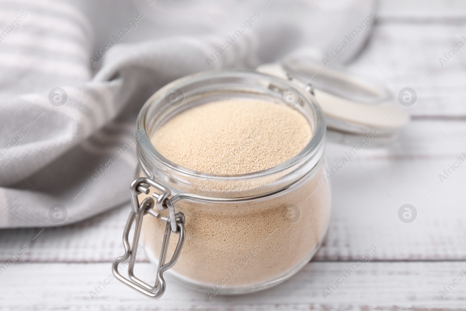 Photo of Granulated yeast in glass jar on white wooden table, closeup