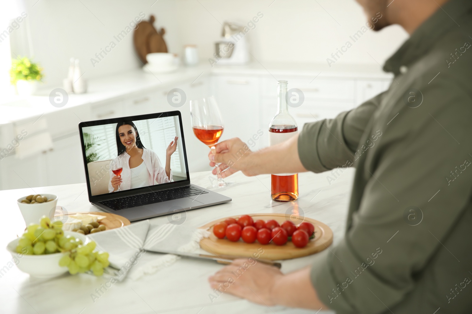 Photo of Friends drinking wine while communicating through online video conference in kitchen. Social distancing during coronavirus pandemic