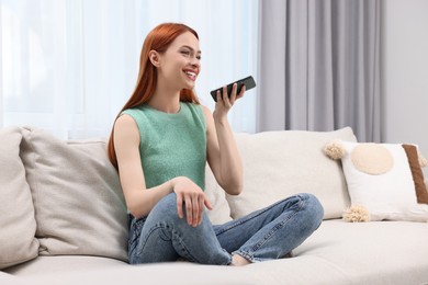 Photo of Happy woman sending voice message via smartphone on couch at home. Space for text