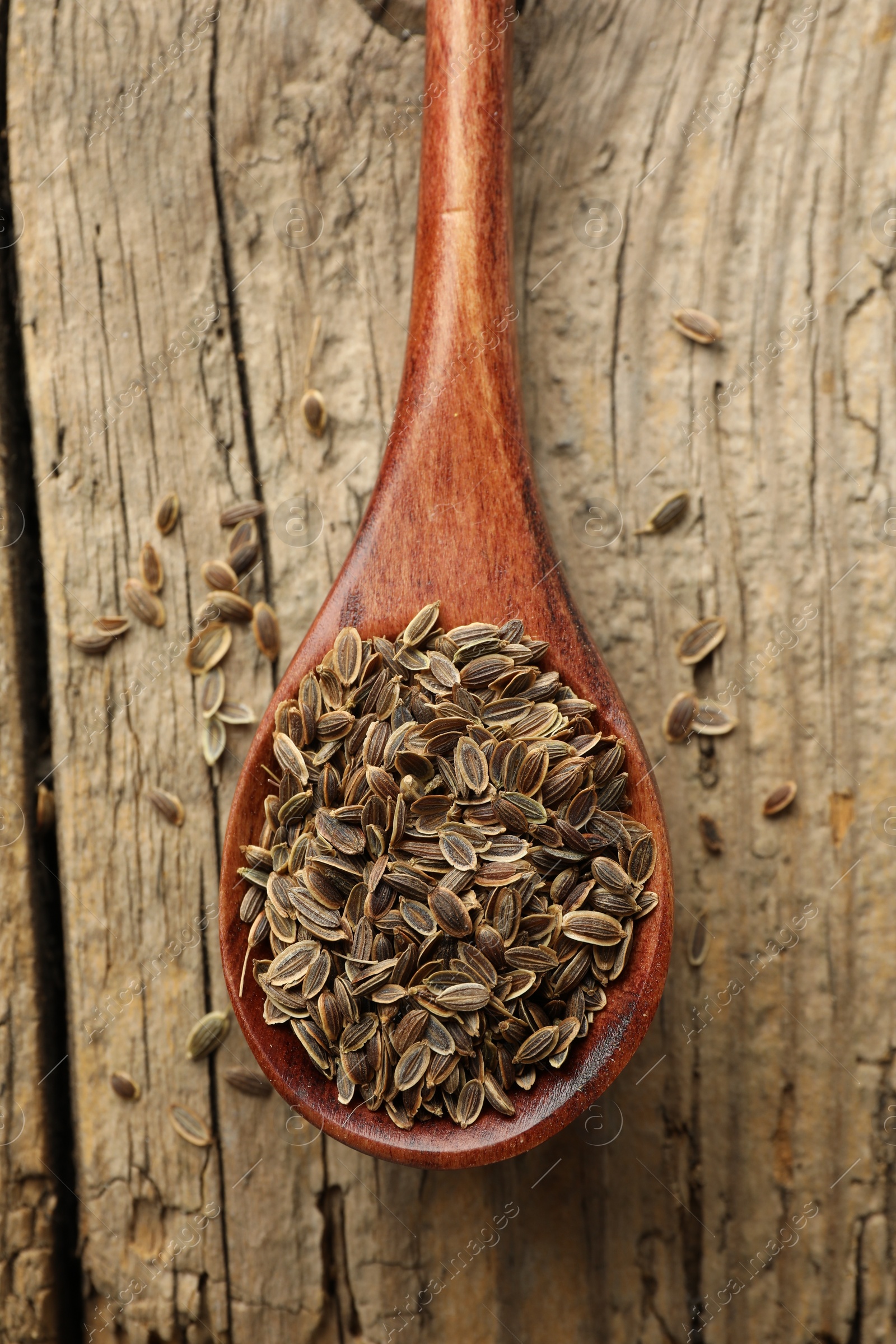 Photo of Spoon of dry dill seeds on wooden table, top view