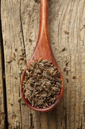 Spoon of dry dill seeds on wooden table, top view