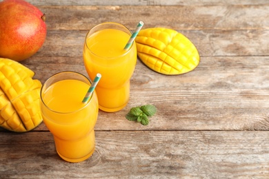 Photo of Fresh tropical mango juice, fruits and space for text on wooden table