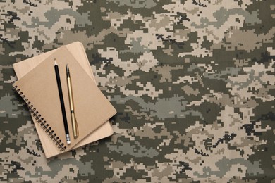 Photo of Notebooks, pen and pencil on camouflage background, top view with space for text. Military education