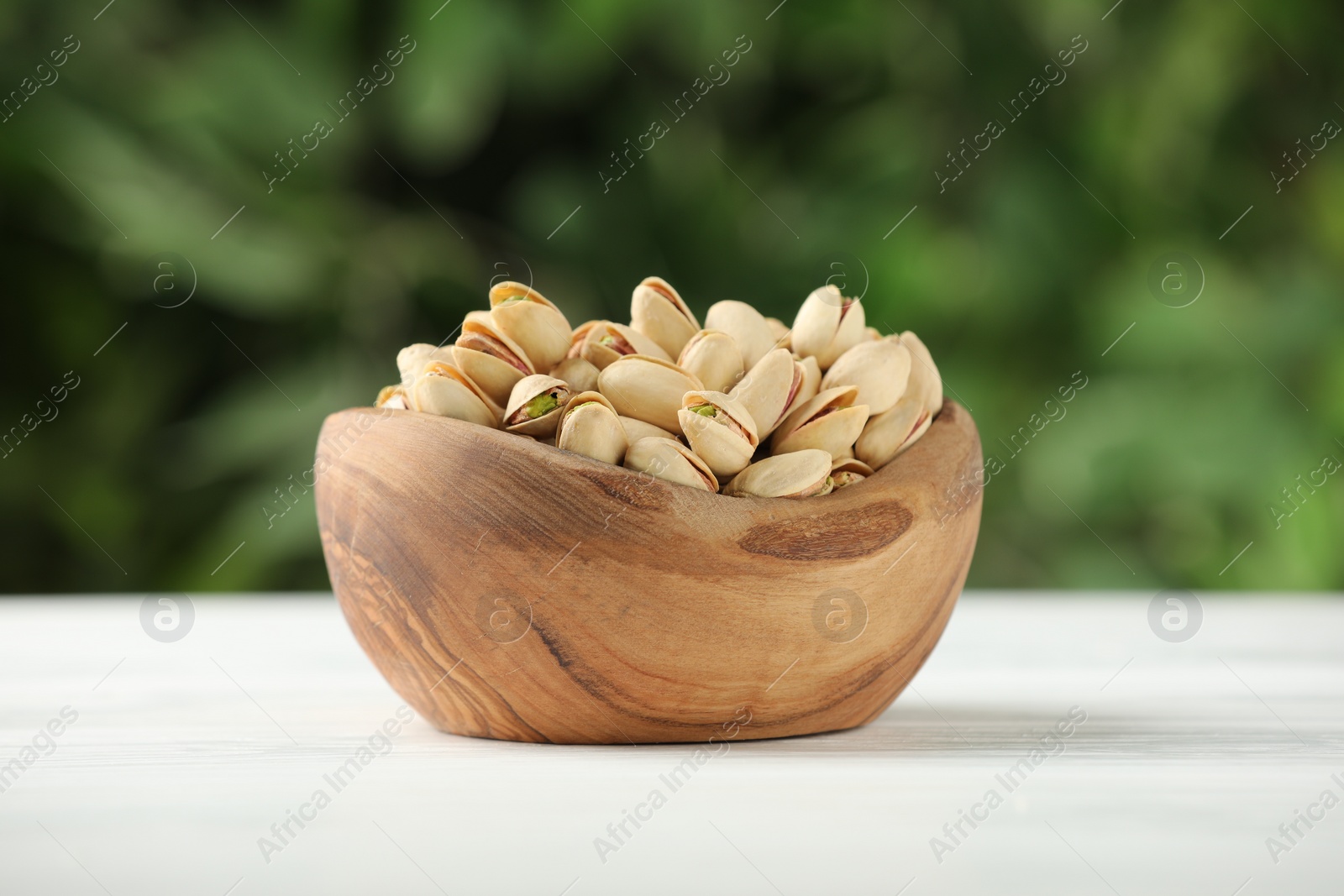 Photo of Tasty pistachios in bowl on white table against blurred background