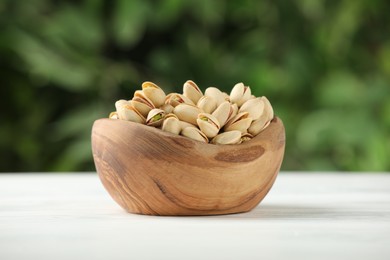 Tasty pistachios in bowl on white table against blurred background