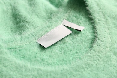 Photo of Blank clothing label on light green sweater, closeup