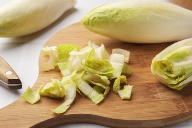 Photo of Fresh raw Belgian endives (chicory) and wooden board on white tiled table, closeup