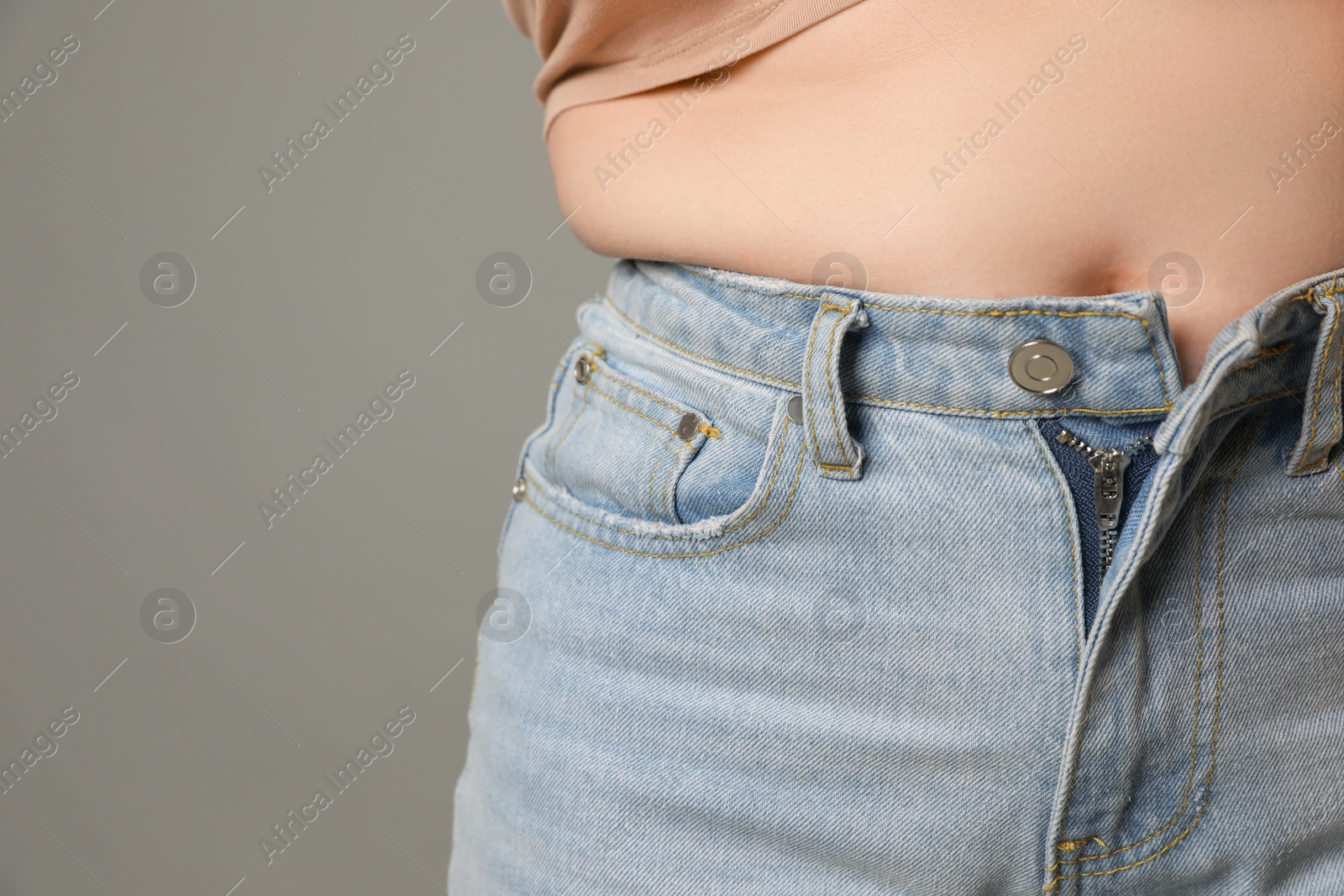 Photo of Overweight woman in tight jeans on grey background, closeup. Space for text