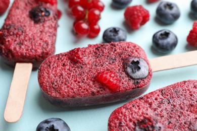 Photo of Tasty berry ice pops on light blue background, closeup. Fruit popsicle