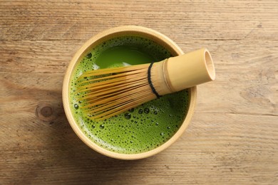 Photo of Cup of fresh matcha tea with bamboo whisk on wooden table, top view