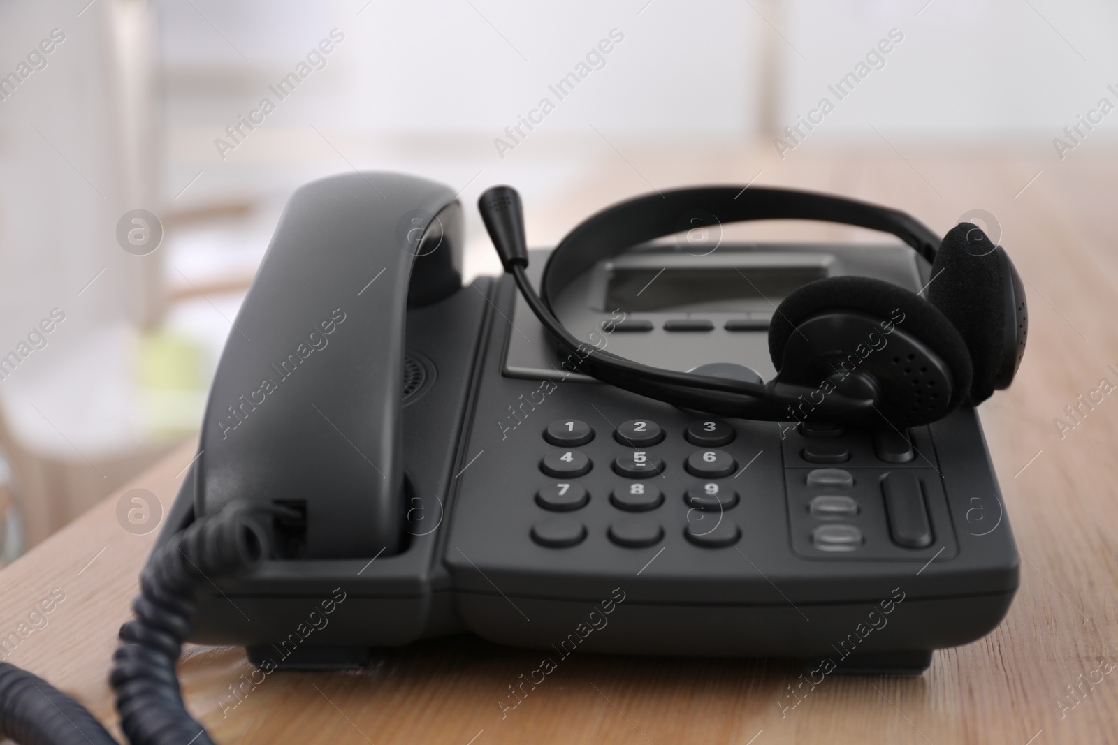 Photo of Office desktop telephone and headset on wooden table. Hotline service