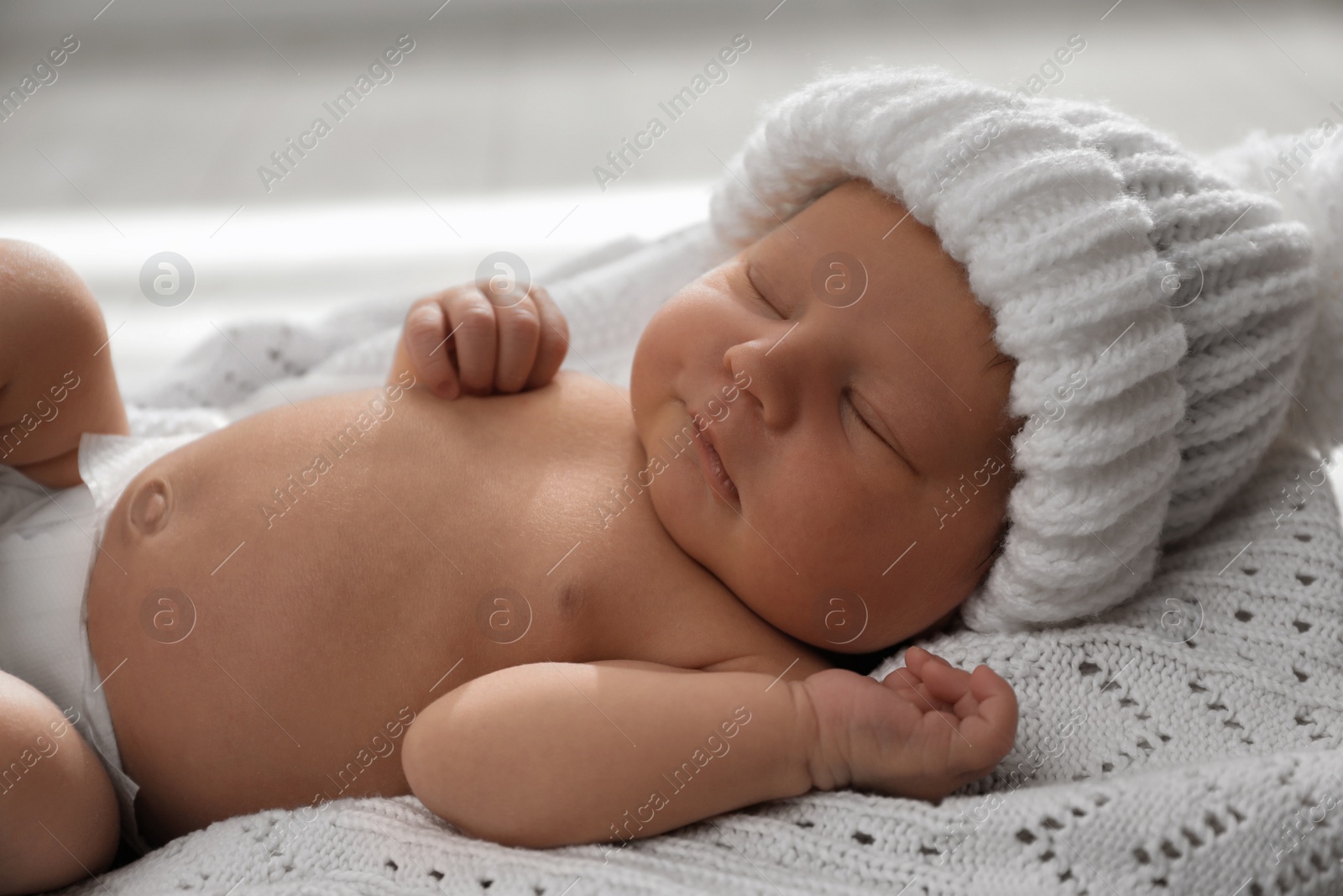 Photo of Cute newborn baby in warm hat sleeping on knitted blanket, closeup