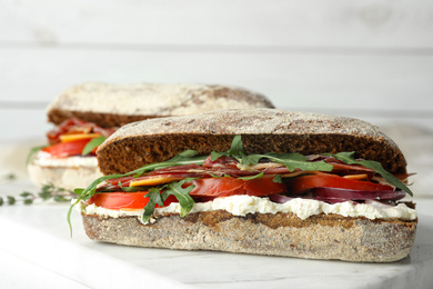 Delicious sandwiches with fresh vegetables and prosciutto on white table, closeup