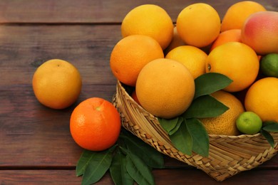 Photo of Wicker basket with different citrus fruits and leaves on wooden table, closeup